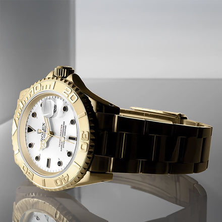 A gold and black luxury wristwatch with a white face displayed on a reflective surface.
