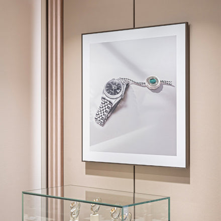 Framed photo of a silver watch and bracelet hangs above a glass display with watches inside.