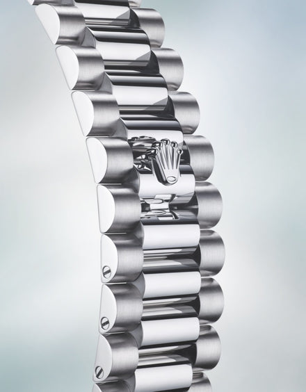 Close-up of a silver metal watch bracelet with a crown-shaped logo on the clasp.