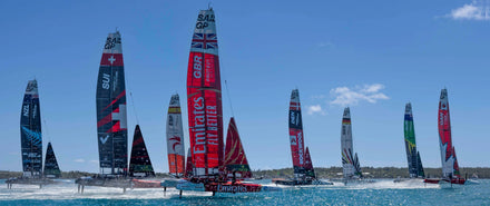 Sailboats from different countries racing together on blue water under a clear sky.