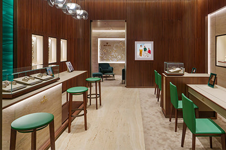 A modern jewelry store interior with wooden walls, green chairs, and display cases showcasing watches.