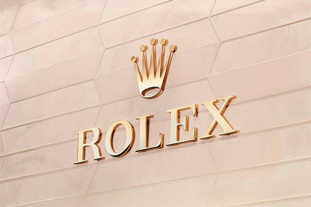 Gold Rolex logo with a crown symbol on a beige, textured wall.