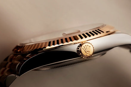 Close-up side view of a luxury wristwatch with a gold crown, fluted bezel, and polished metal case.