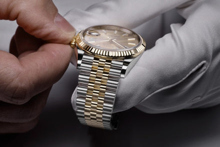 A gloved hand adjusts the crown of a two-tone gold and silver wristwatch with a fluted bezel.