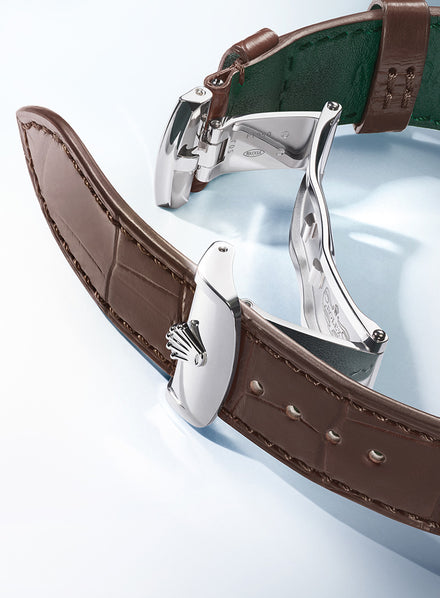 Close-up of a brown leather watch strap with a polished silver clasp featuring a crown logo.