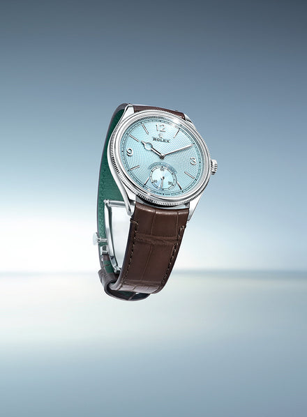 A silver Rolex watch with a light blue face and brown leather strap, set against a gradient blue background.