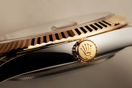 Close-up of a luxury watch crown with the Rolex logo, showing gold and stainless steel details.