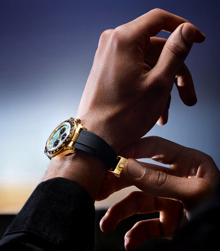 A person adjusts a gold wristwatch with a black strap on their wrist against a blurred background.