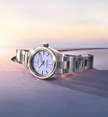 A silver wristwatch with a white face on a flat surface, with a soft sunset background.