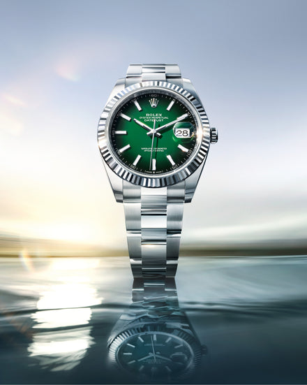 Silver watch with a green face on a reflective surface with a blurred background