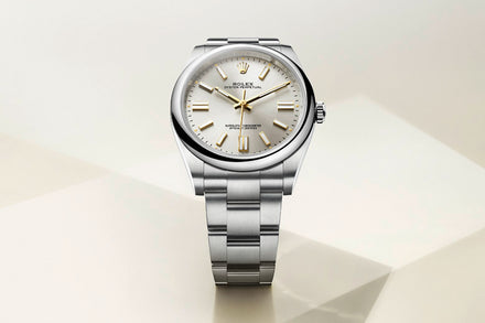 A silver Rolex wristwatch with a white face and gold hour markers, displayed on a light geometric background.