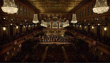 A grand concert hall with chandeliers, ornate ceiling, and an orchestra performing on stage.