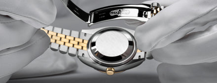 Gloved hands holding the back and clasp of a two-tone Rolex watch.