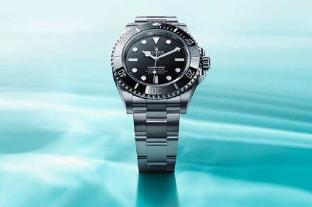 Silver Rolex watch with a black dial displayed above a light blue water-like background.