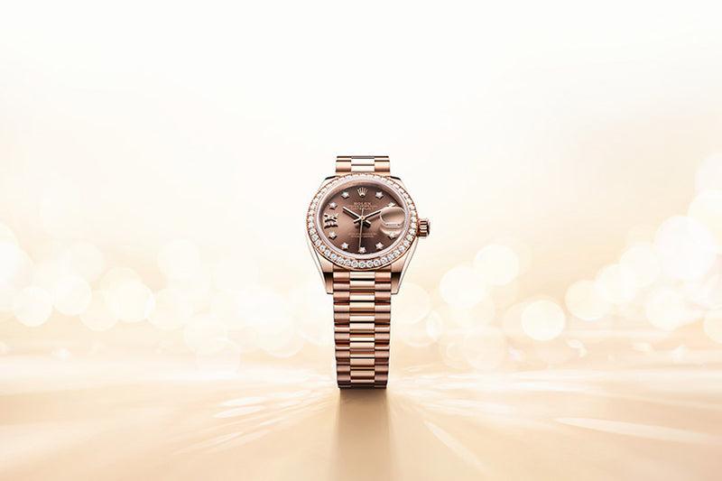 Rose gold luxury wristwatch with a diamond bezel on a reflective, light-filled beige background.