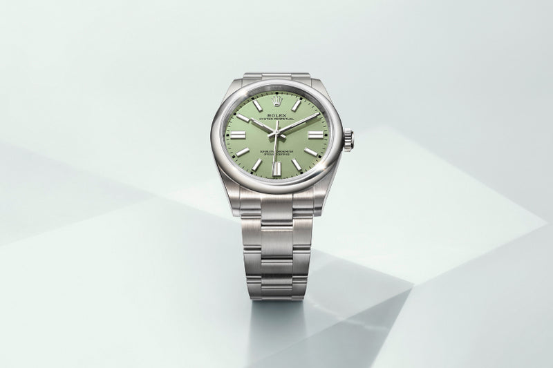 A silver Rolex wristwatch with a green dial displayed on a light, geometric background.