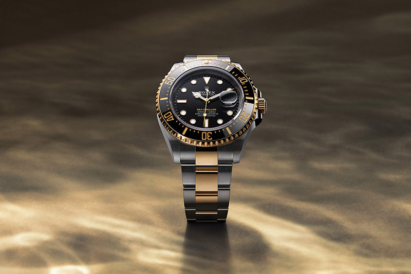 A two-tone gold and silver Rolex watch with a black dial displayed on a gold-toned surface.
