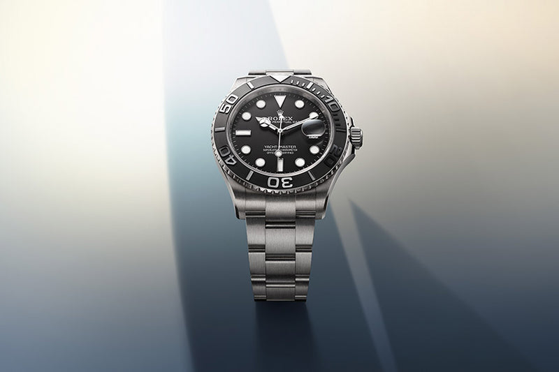 A silver Rolex dive watch with a black dial and bezel is displayed on a gradient background with soft shadows.