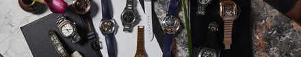 A variety of watches scattered across a marble background and a leather booklet 