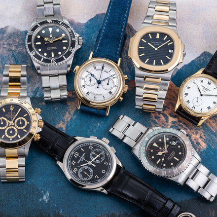A selection of watches from various brands and in different colors and strap materials set side by side with a photo printed background
