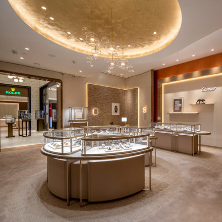 Luxury jewelry store interior with glass display cases, elegant lighting, and Cartier and Rolex sections visible.