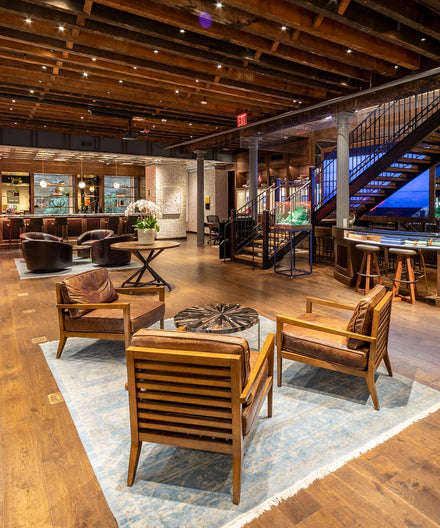 Hotel lobby with wood floors, leather chairs, blue rug, staircase, and exposed wooden ceiling beams.