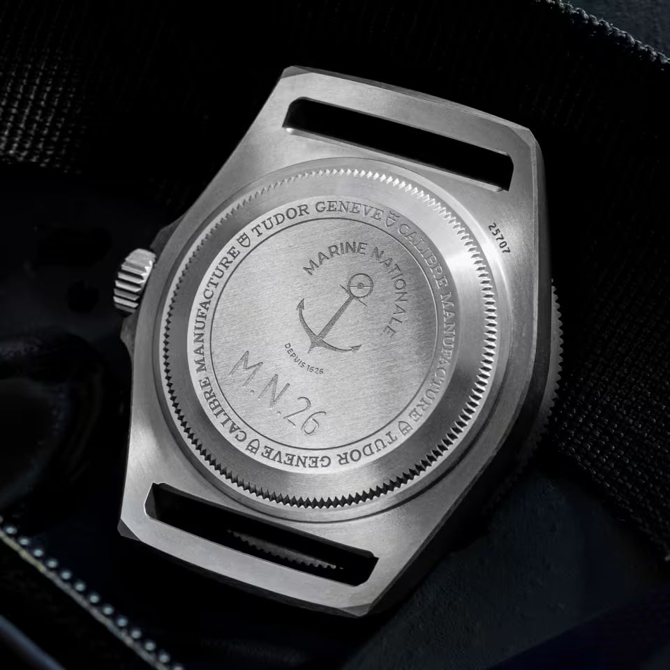 Close-up of a silver watch case with 'Tudor Geneve' branding on a dark background