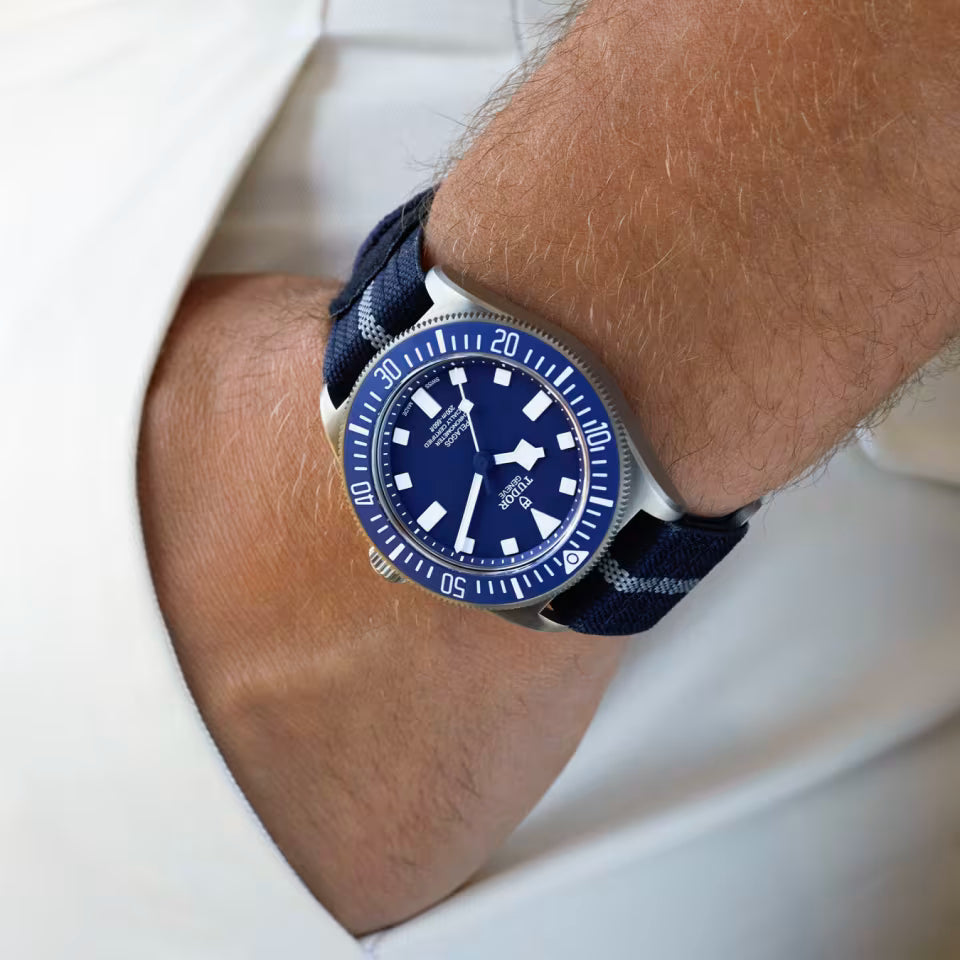 Blue wristwatch with a navy strap on a person's wrist against a white background