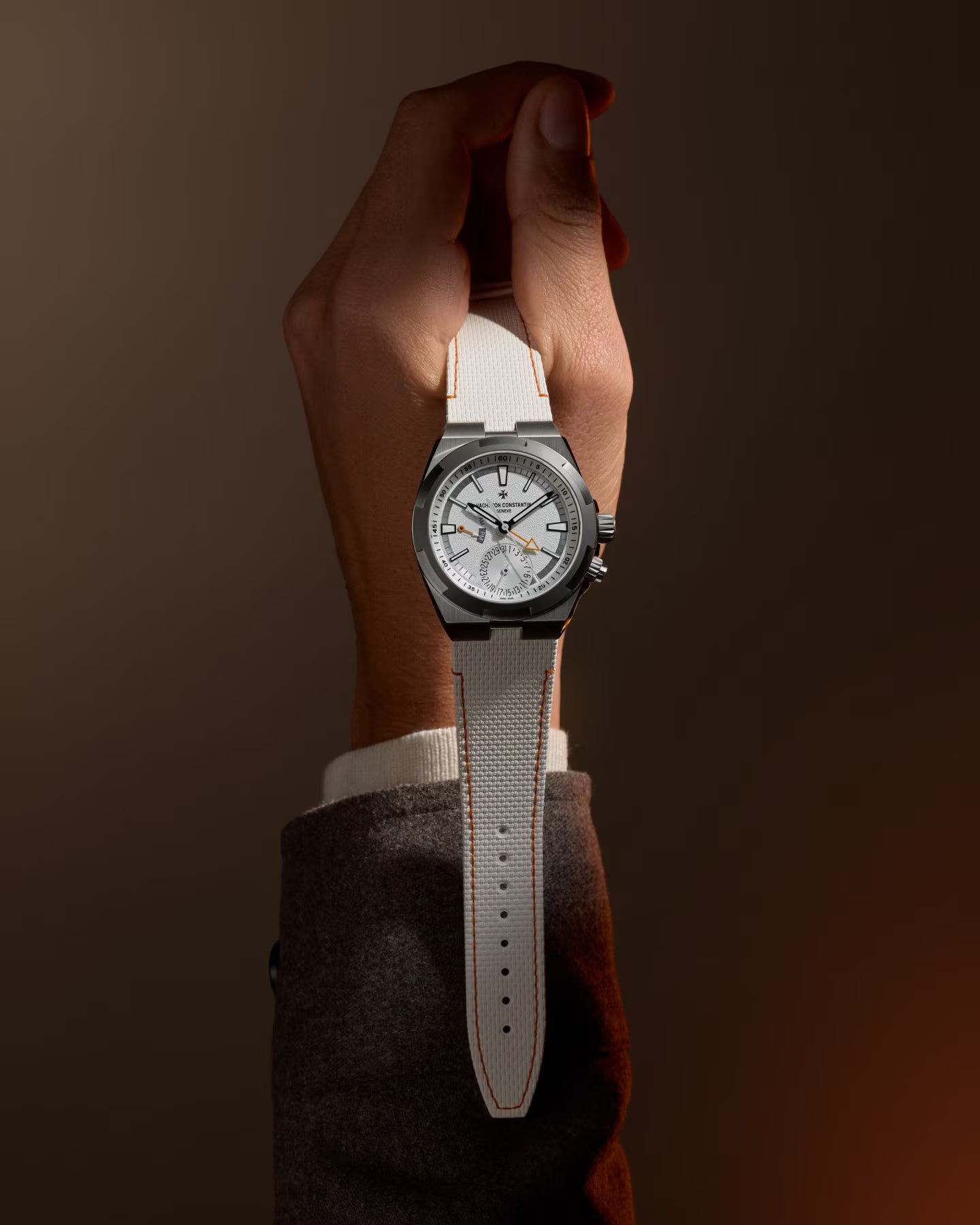 Wristwatch with white dial, cardinal point markers, dual time display, and light gray fabric strap worn on wrist.