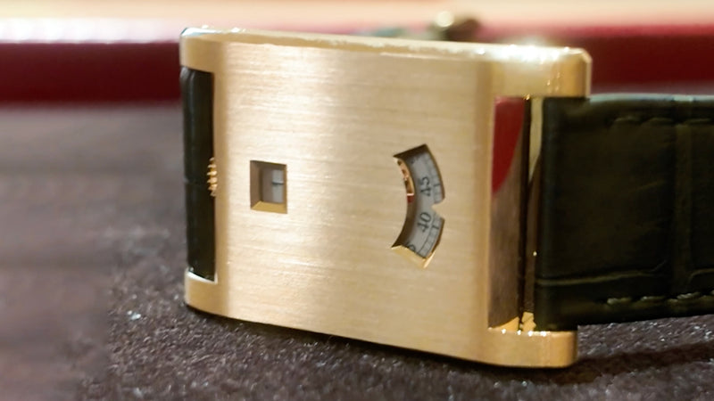 Rectangular gold watch with a black strap, showing digital hour and minute windows on its brushed metal face.